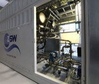 Foto eines großen Metallcontainers mit geöffneter Tür. Darinnen ist der eigentliche Elektrolyseur zu sehen.