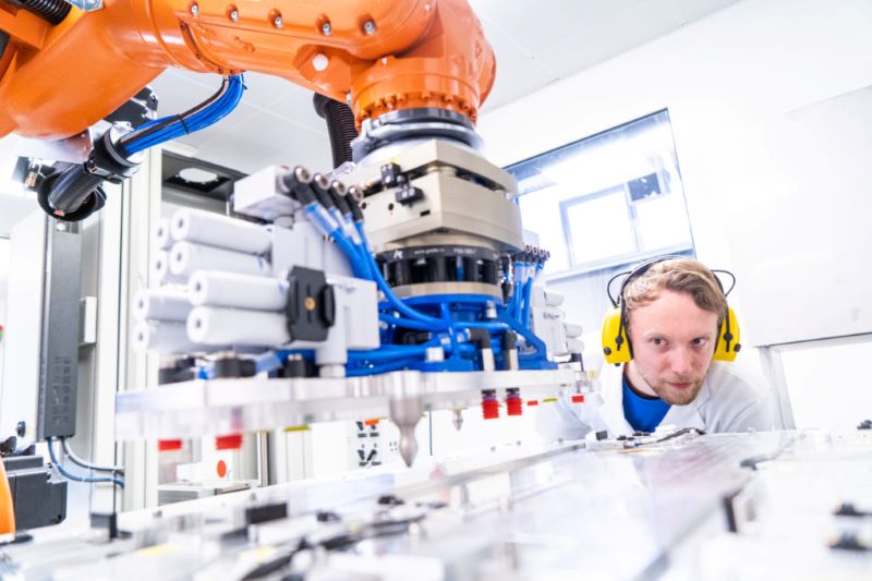 Ein Forscher beobachtet eine automatisierte Fertigung unter einem Roboterarm.