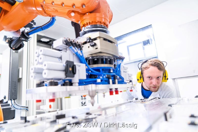 Ein Forscher beobachtet eine automatisierte Fertigung unter einem Roboterarm.