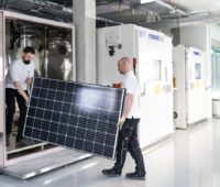 Zu sehen sind zwei Forscher mit einem Modul im Testzentrum für die potenzialinduzierte Degradation von Photovoltaik-Modulen beim ZSW.