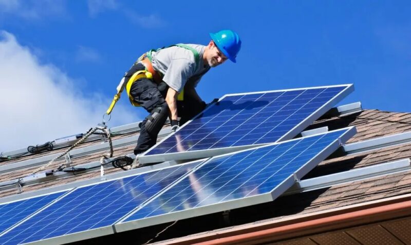 Im Bild ist ein Monteur auf dem Dach bei der Photovoltaik Installation zu sehen, der Betreiber profitiert von der Nullsteuer.