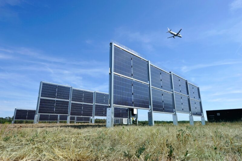 Senkrecht stehende Solarpanels unter einem abhebenden Flugzeug