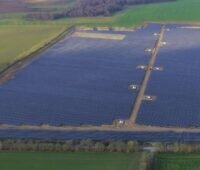 Luftbild einer großen PV-Freiflächenanlage auf grüner Wiese.