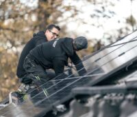 Zwei Handwerker bei der Montage von Solarmodulen auf einem Satteldach.