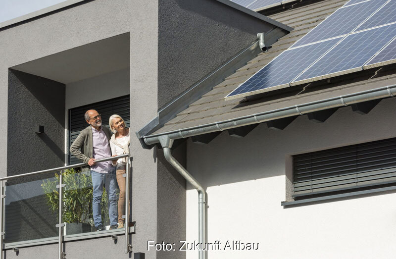 Älteres Paar betrachtet vom Balkon aus PV-Anlage auf dem Dach