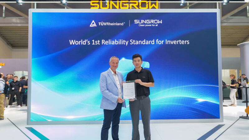 Zwei Vertreter von TÜV Rheinland und Sungrow präsentieren auf einem Messestand ein Zertifikat für neue Zuverlässigkeitsstandards von PV-Wechselrichtern. Im Hintergrund ist eine große Bildschirmwand mit den Logos beider Unternehmen zu sehen.