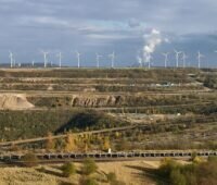 Hinter den Schluchten ehemaliger Braunkohleschächte erhebt sich eine Reihe Windkraftanlagen.