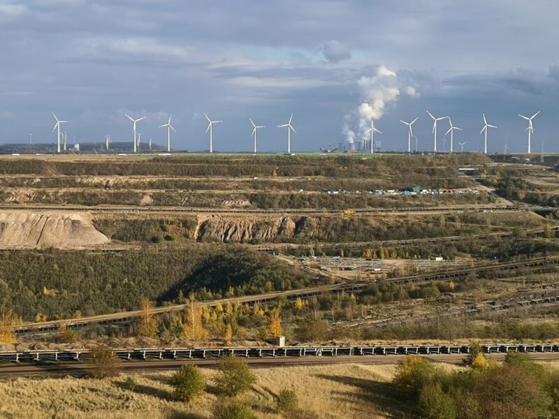 Hinter den Schluchten ehemaliger Braunkohleschächte erhebt sich eine Reihe Windkraftanlagen.