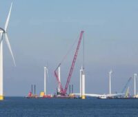 Ein Kran und Windenergieanlagen im Meer, die Offshore-Wind-Branche fordert bessere Rahmenbedingungen.