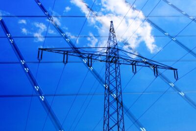 Ein Strommast (und eine Wolke) spiegeln sich in einem Photovoltaik-Modul. Im Projekt PV-MoVe geht es um bessere Wechselrichter.
