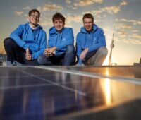 Dreio Männer in blauen Pullis hinter Solarmodulen auf dem Dach und vor Sonnenuntergang in Berlin.