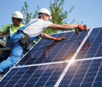 Zwei Handwerker schrauben Photovoltaikmodule an einem Dachfirst fest
