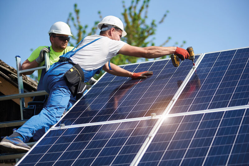 Zwei Handwerker schrauben Photovoltaikmodule an einem Dachfirst fest