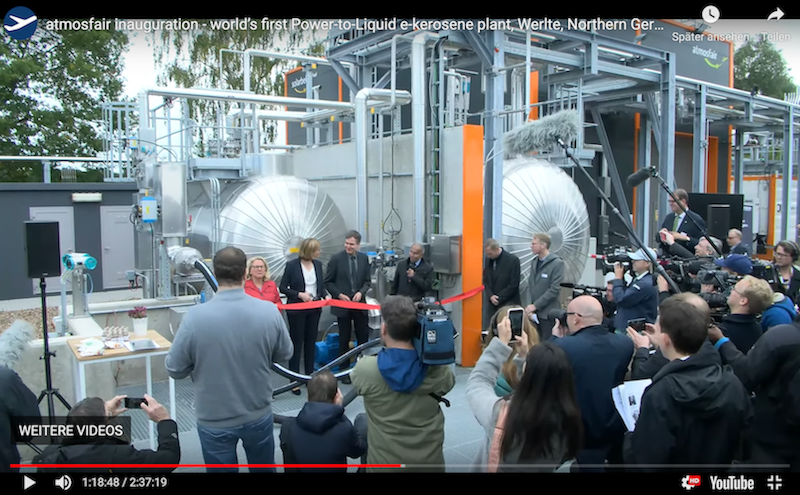 Blick durchs Publikum auf mehrere Personen, die ein rotes Band vor einer Industrie-Anlage durchschneiden: Einweihung der E-Fuel Fertigung