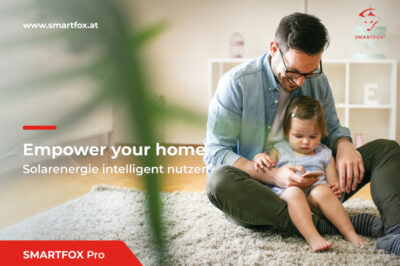Smartfox: Enpower your home. Solarenergie intelligenz nutzen. Zu sehen ist ein auf einem Teppich sitzender Mann mit Mädchen auf dem Schoß, der auf ein Smartphone blickt und lacht.