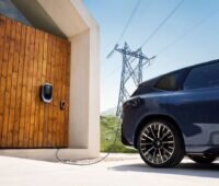 Elektrofahrzeug im Freienb an der Wallbox mit Hochspannungsmast in Sichtweite.