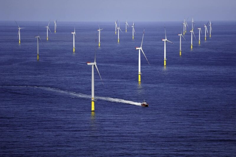 Ein Offshorewindpark bei ruhiger See. Ein Schiff manövriert hindurch.