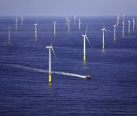 Ein Offshorewindpark bei ruhiger See. Ein Schiff manövriert hindurch.