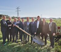 Männergruppe auf einem Feld nehmen Spatenstich für Bürgerwindpark vor mit übergroßem Sparen