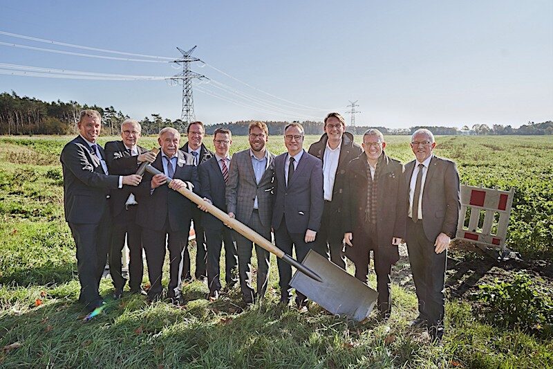 Männergruppe auf einem Feld nehmen Spatenstich für Bürgerwindpark vor mit übergroßem Sparen