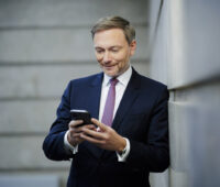 Bundesfinanzminister Lindner lehnt an einer Wand und schaut in sein Smartphone. Er hat das Wachstumschancengesetz vorgeschlagen.
