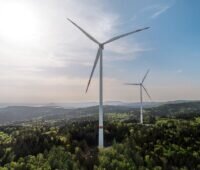 Zwei Windkraftanlagen in einer Hügellandschaft.