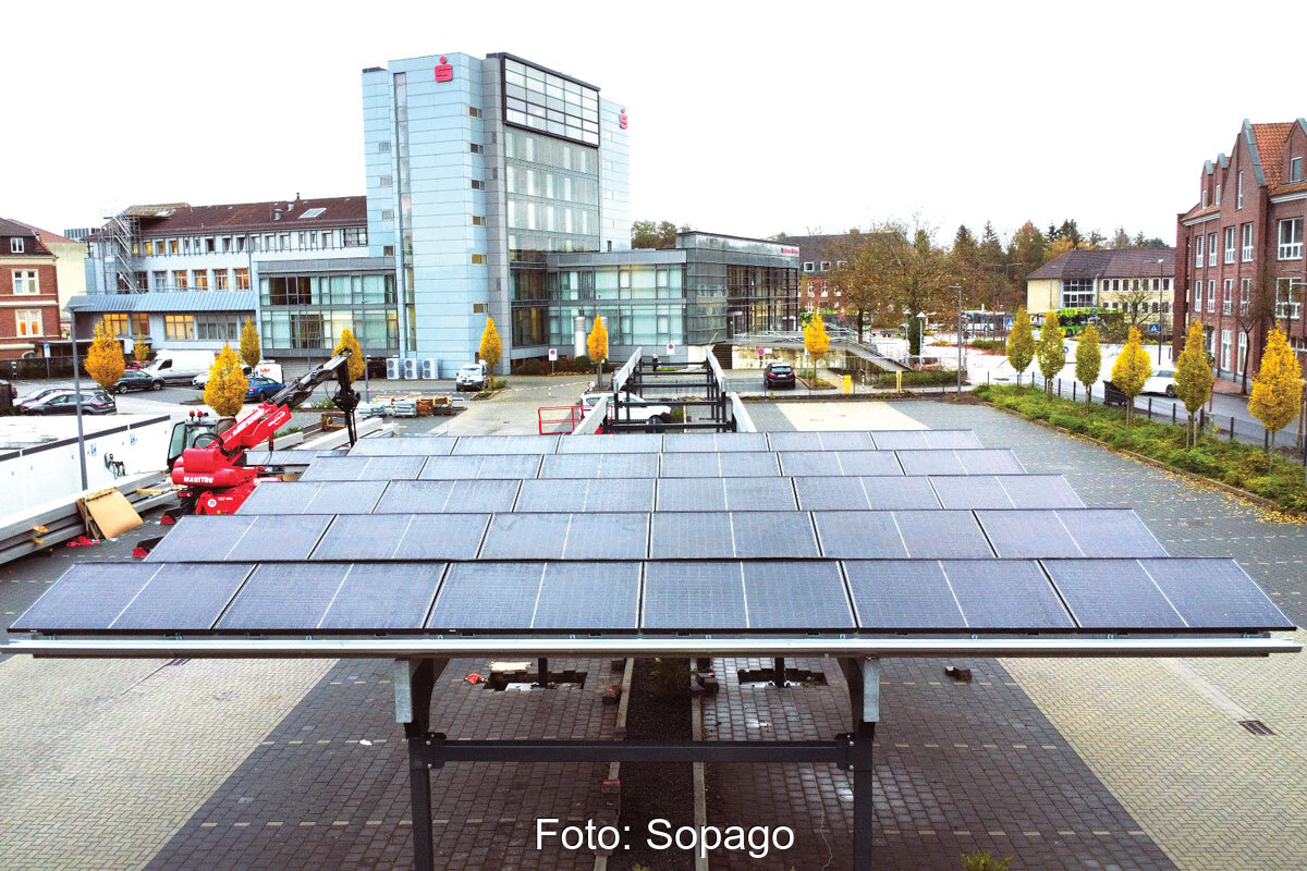 Solarcarport auf einem Parkplatz. Im Hintergrund das Gebäude der Sparkasse.