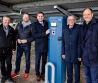 Fünf Männer mit dunklen Anzügen neben blauer Ladesäule - Ladepunkte für E-Autos in Norddeich