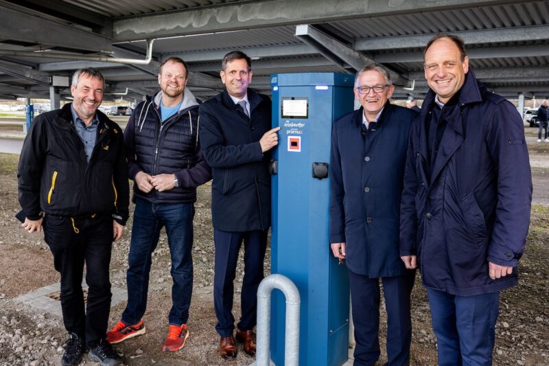 Fünf Männer mit dunklen Anzügen neben blauer Ladesäule - Ladepunkte für E-Autos in Norddeich