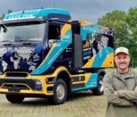 Tobias Wagner steht vor dem blau-orange folierten Elektro-Lkw eActros 600 mit Wohnmobil-Aufbau und Weltkartenmotiv.
