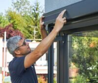Ein Monteur bringt ein rechteckiges Solarmodul an einem Fenstersichtschutz an.