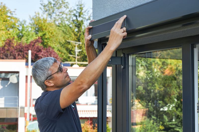 Ein Monteur bringt ein rechteckiges Solarmodul an einem Fenstersichtschutz an.
