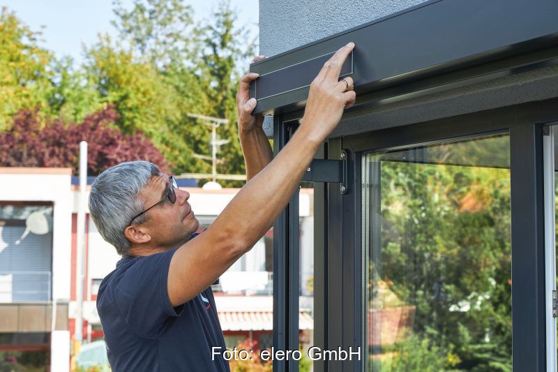 Ein Monteur bringt ein rechteckiges Solarmodul an einem Fenstersichtschutz an.