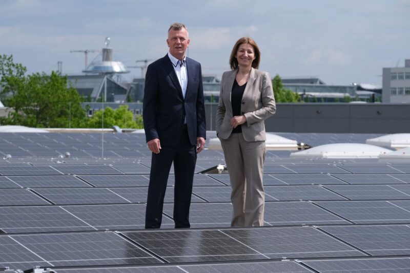 Eine Frau udn ein Mann im Business-Outfit auf dem Dach eines Unternehmens mit PV.