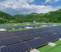 Ein Flachdach mit PV-Elementen vor hügeligem grünen Hintergrund.