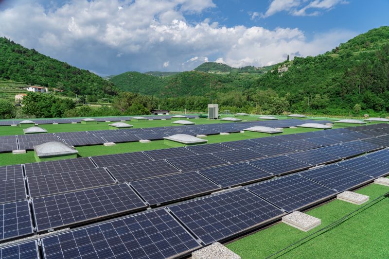 Ein Flachdach mit PV-Elementen vor hügeligem grünen Hintergrund.