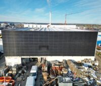 Vollflächige Solarfassade eines Bestrandgebäudes, davor Baufahrzeuge.