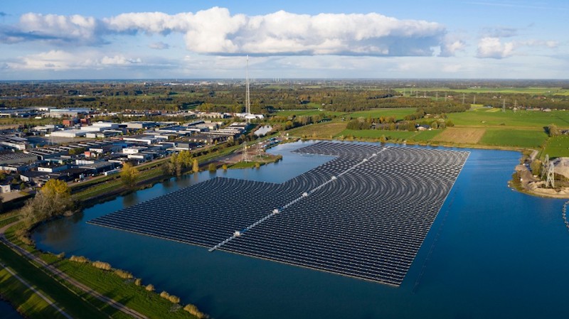 Solarmodule schwimmen auf einem See in den Niederlanden.. Links vom See befindet sich ein Industriegebiet, im Hintergrund Grünland.
