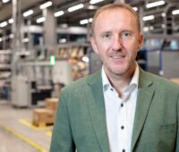Beim Wechselrichter-Hersteller Fronius: Ein Mann mit grau-grünem Jacket in einer Lagerhalle schaut in die Kamera