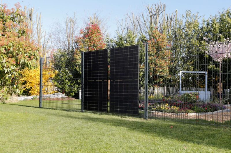 Zwei hochkant stehende PV-Module integriert in einen Zaun in blühendem Garten.