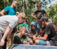 Mädchen und Jungen vor einem PV-Modul umgeben von Dschungel.