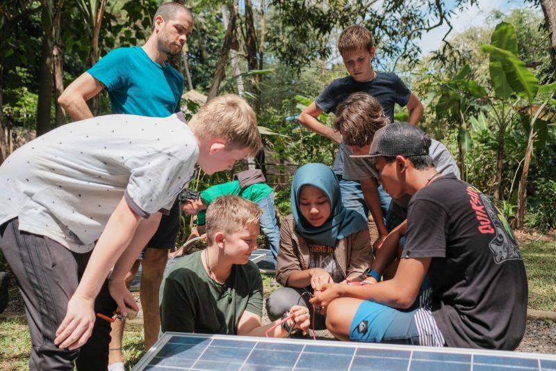 Mädchen und Jungen vor einem PV-Modul umgeben von Dschungel.