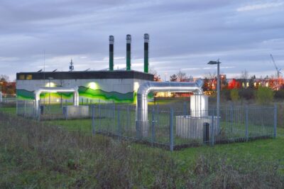 Beleuchtetes Heizkraftwerk nach Sonnenuntergang mit Rohren, die in den Untergrund führen.