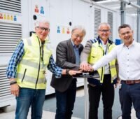 Vier Personen drücken symbolisch für die Inbetriebnahme auf einen Knopf. Die Hände liegen übereinander.