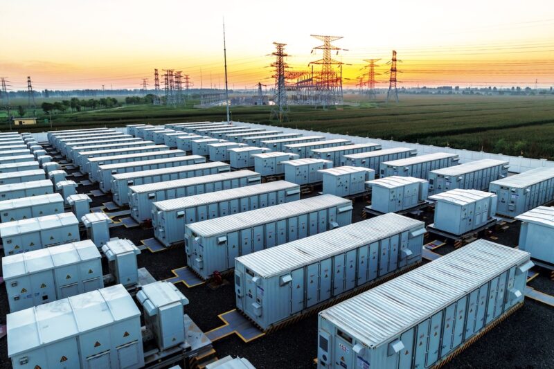 Mehrere Reihen mit Containern (Großspeicher), im Hintergrund Hochspannungsmasten