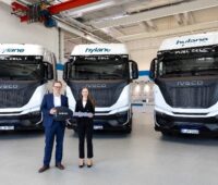 Christian Sulser (Vorstandsvorsitzender, Iveco Magirus AG) übergibt die Fahrzeuge an Dr. Sara Schiffer (Geschäftsführerin, Hylane GmbH). Im Hintergrund stehen die drei Sattelzugmaschinen.
