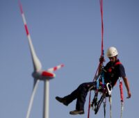 Zu sehen ist ein Arbeiter, der an einer Windenergieanlage hängt. Frauen sind in den Erneuerbaren Energien unterrepräsentiert.