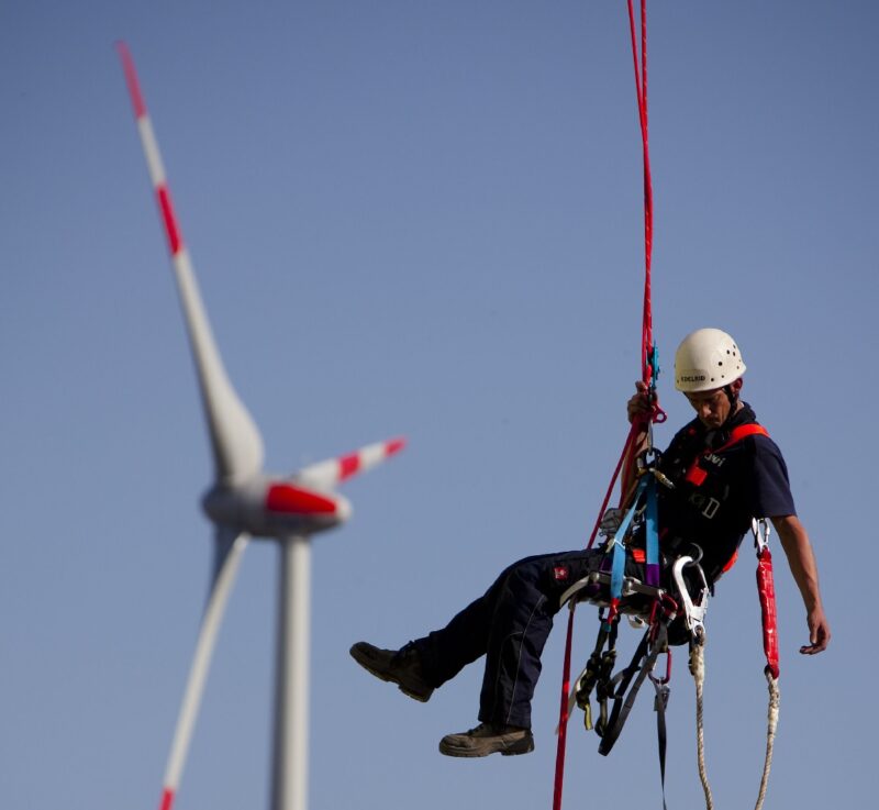 Zu sehen ist ein Arbeiter, der an einer Windenergieanlage hängt. Frauen sind in den Erneuerbaren Energien unterrepräsentiert.