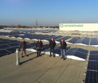 Vier Männer auf einem Hallendach mit PV ringsum.