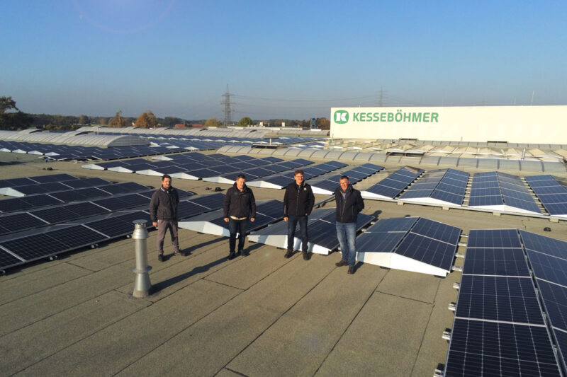 Vier Männer auf einem Hallendach mit PV ringsum.